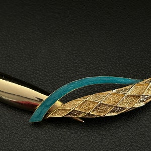 May include: A gold and teal blue statement necklace with a geometric design. The necklace is made of metal and has a textured finish.