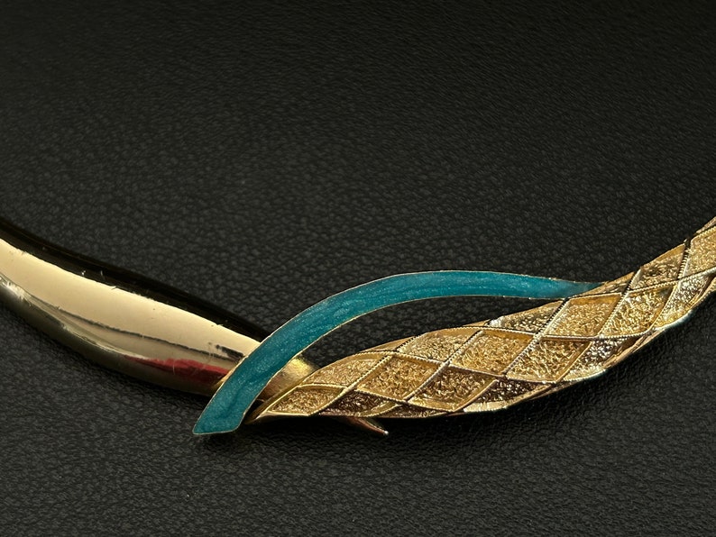 May include: A gold and teal blue statement necklace with a geometric design. The necklace is made of metal and has a textured finish.