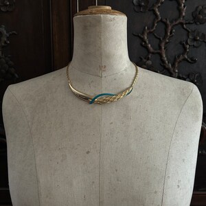 May include: A gold and teal blue statement necklace with a woven design. The necklace is displayed on a white mannequin.
