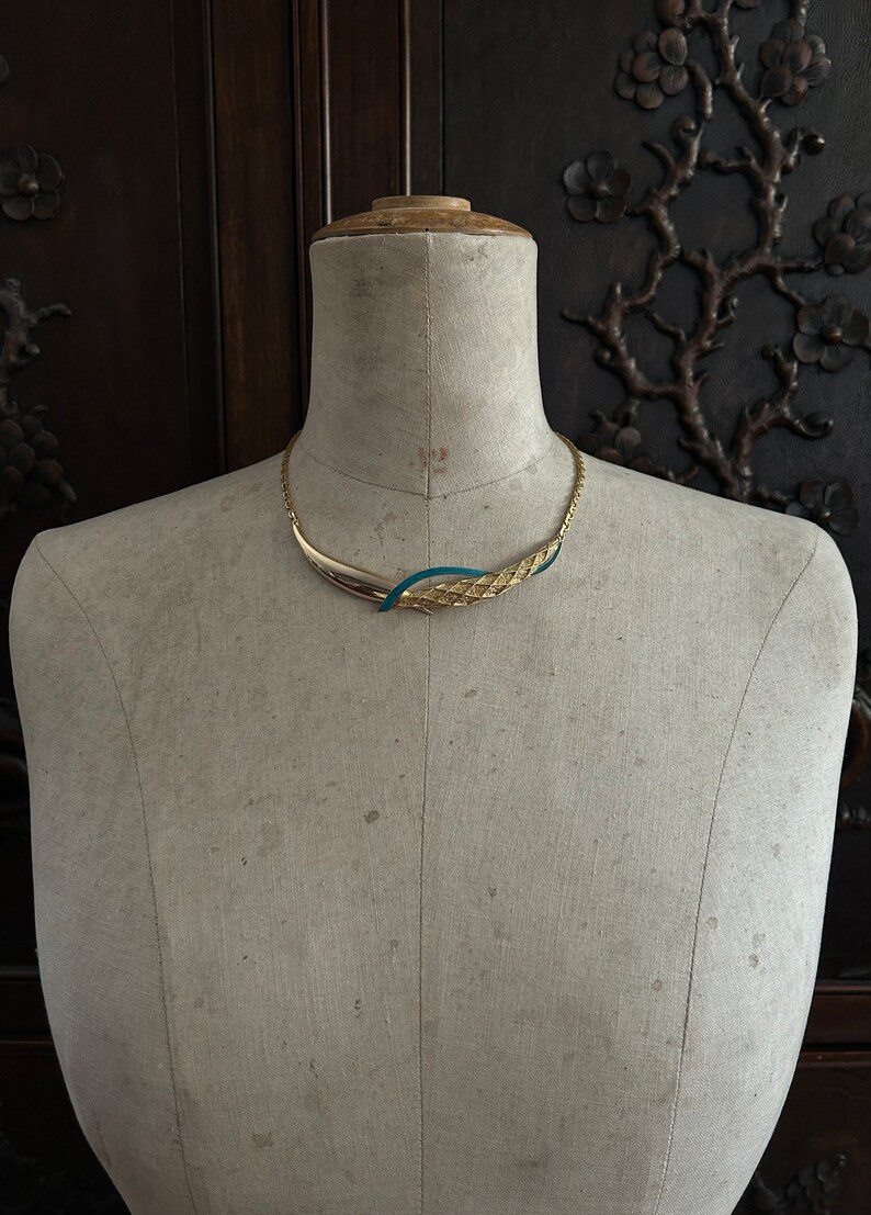 May include: A gold and teal blue statement necklace with a woven design. The necklace is displayed on a white mannequin.
