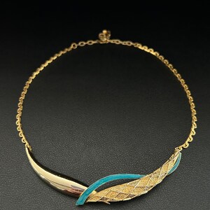 May include: A gold chain necklace with a blue and gold pendant. The pendant is a curved design with a textured gold surface and a blue enamel accent.