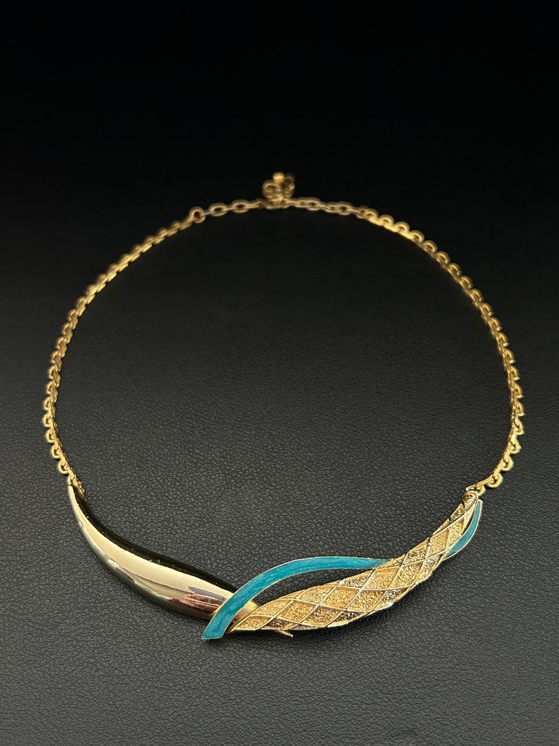 May include: A gold chain necklace with a blue and gold pendant. The pendant is a curved design with a textured gold surface and a blue enamel accent.