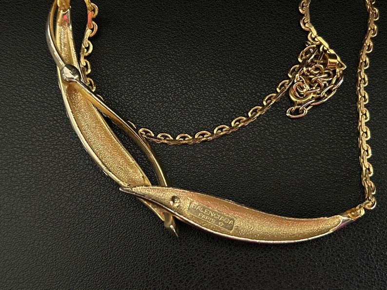 May include: A gold-toned necklace with a crescent-shaped pendant. The pendant has the text "BALENCIAGA PARIS" engraved on the back.