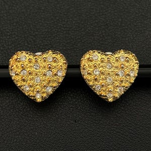 Könnte beinhalten: Ein Paar goldene herzförmige Ohrringe mit klaren Strasssteinen.