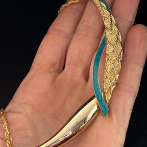 May include: A gold tone necklace with a turquoise blue enamel design. The necklace has a chain link style and a unique pendant with a curved shape.