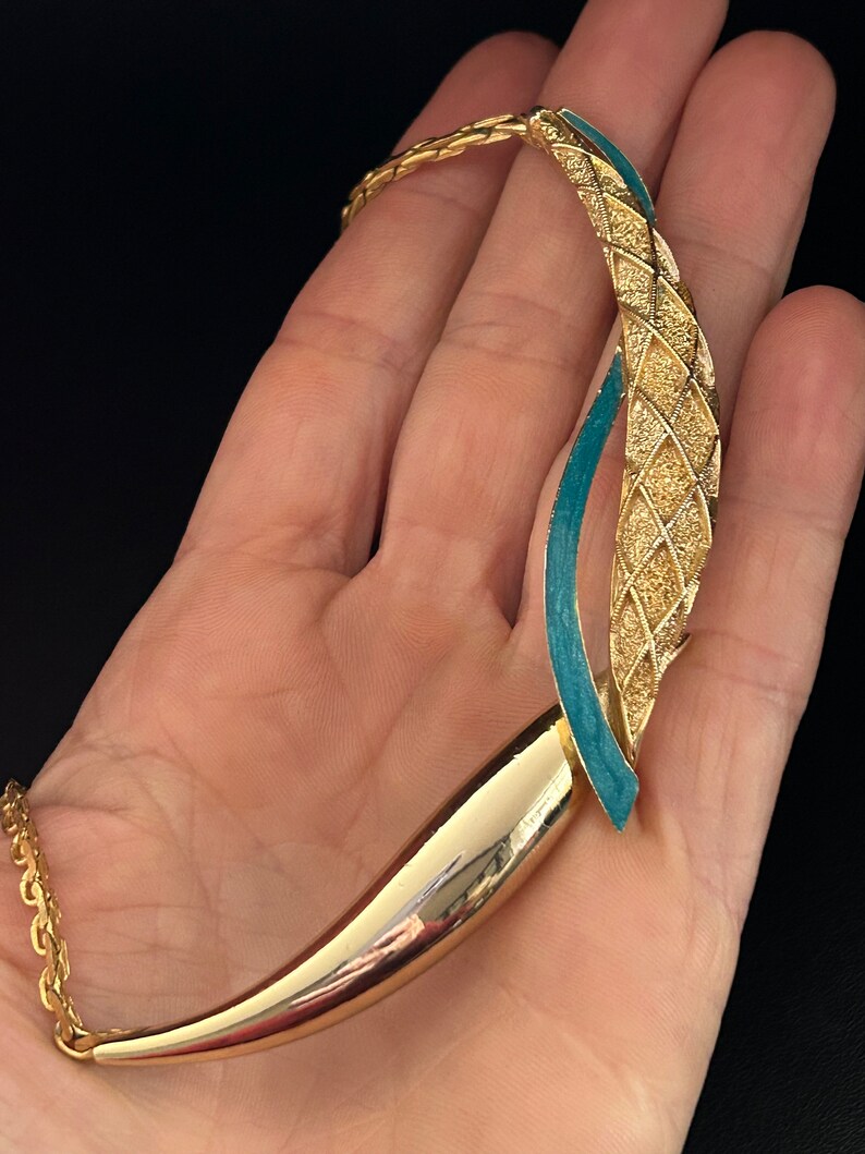 May include: A gold tone necklace with a turquoise blue enamel design. The necklace has a chain link style and a unique pendant with a curved shape.