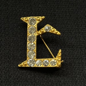 Broche L en tono dorado Lancome