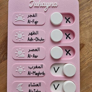 Peut inclure: Un tableau rose Juhayna avec du texte arabe et des traductions anglaises. Il comporte cinq sections avec des icônes de soleil et de lune, des interrupteurs à bascule et des coches. Le tableau est conçu pour suivre les activités quotidiennes.