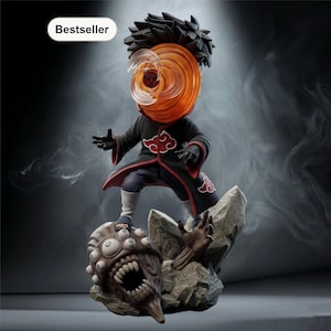 May include: A detailed figurine of a character from an anime series. The figure is wearing a black cloak with red cloud designs and an orange mask. The figure is standing on a rock formation with a monster base. The word "Bestseller" is in the top left corner.