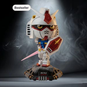 May include: A white, red, and blue Gundam figurine with a shield and a pink energy sword. The figurine is on a rocky base with the text "RX-78-2 GUNDAM". A "Bestseller" label is in the upper left corner.