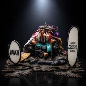 May include: A detailed figurine featuring a male character with an eyepatch and a female character with a skull headpiece, both seated. Two white oval signs are present, one reading BANKAI and the other reading KATEN KYOKOTSU KARAMATSU SHINJU.