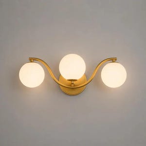 May include: A gold-toned wall sconce with three spherical, frosted glass shades. The fixture has a curved design and is mounted on a circular base. The light fixture is designed for indoor use.