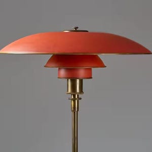 Könnte beinhalten: Eine Stehlampe im Mid-Century-Modern-Stil mit einem mehrschichtigen, roten Schirm und einem messingfarbenen Stiel. Die Lampe hat ein unverwechselbares Design mit einem großen, geschwungenen oberen Schirm und kleineren, darunter gestapelten Schirmen. Gesamthöhe ca. 152 cm.