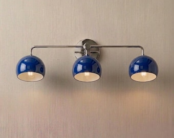 May include: A three-light vanity fixture with a polished chrome finish. The fixture features three deep blue, spherical shades with white interiors. The lights are mounted on a horizontal bar and a circular backplate.