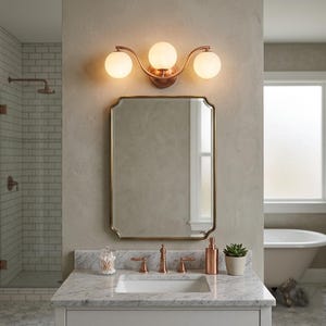 May include: A bathroom vanity with a copper-toned three-light fixture above a rectangular mirror with a gold frame. The vanity has a marble countertop with a sink, faucet, and accessories. A shower and a bathtub are visible in the background.