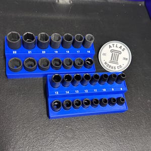 May include: Two blue plastic socket organizers holding black metal sockets. The top organizer holds sizes 16 through 22, and the bottom holds sizes 8 through 15. A circular white sticker with the text Atlas Works Co. Est. 2028 is placed nearby.
