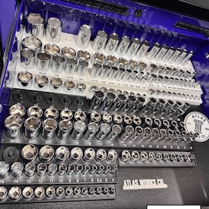 May include: A blue metal tool chest drawer containing white and black plastic organizers filled with various chrome-plated steel socket sets. The organizers feature printed numerical size labels. A circular sticker reads Atlas Works Co.
