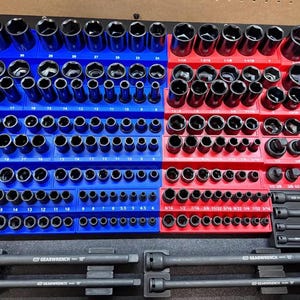 May include: A collection of black metal socket tools organized on blue and red plastic storage trays. The set includes various sizes of sockets, extensions, and adapters. A small white rectangular sign states Tools NOT Included in black text.