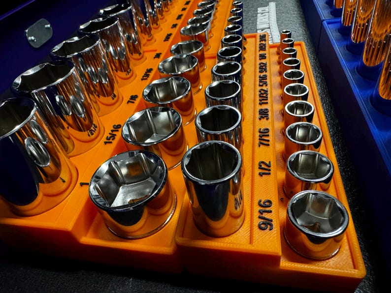 May include: A collection of polished chrome sockets neatly arranged in an orange organiser. The sockets are of different sizes, with measurements such as 9/16, 1/2, and 7/16 clearly marked. The organiser is placed inside a blue container.
