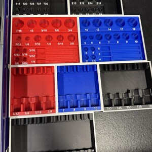 May include: A set of black, red, and blue socket organizers with various sizes and labels. The organizers are arranged in a tray, with sizes including 1/8, 1/4, 5/16, and 3/8 inches. The labels include T40, T45, T50, T55, and T60.