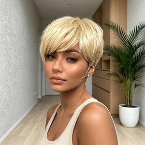 Op de afbeelding: Een korte, gelaagde blonde pruik met een zijwaartse pony en een getextureerde, volumineuze styling. Het haar heeft een lichte, heldere platinablonde tint met subtiele donkere aanzet en is gestyled in een modern, kort kapsel.