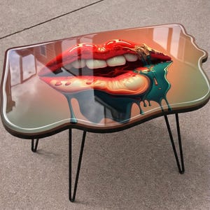 May include: A unique coffee table featuring a glossy surface with a vibrant image of red lips with white teeth and dripping teal paint. The table has a dark brown edge and black hairpin legs, adding a modern touch to the design.