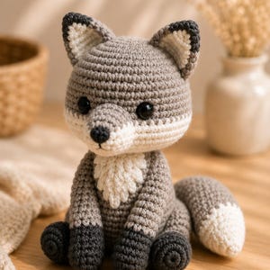 May include: A handcrafted crochet fox toy featuring a grey body, dark grey paws, and a white chest patch. The fox has pointed ears with white inner details, black plastic eyes, and a bushy tail with a white tip, all worked in a dense yarn stitch.