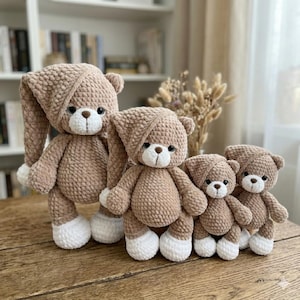 May include: Four handmade crochet teddy bears in varying sizes. The bears are a soft brown color with white feet and a matching hat. The bears have black eyes and a white muzzle. The bears are standing in a row.