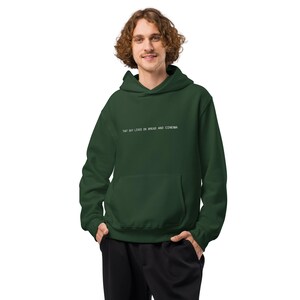 Op de afbeelding: Een donkergroene hoodie met een voorzak en een capuchon met trekkoord. De tekst "THAT GUY LIVES ON BREAD AND CINEMA" is in het wit op de borst gedrukt. De hoodie is gemaakt van een zacht, comfortabel materiaal.