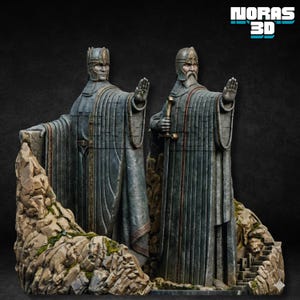 Puede incluir: Dos estatuas de figuras vestidas con túnicas con las manos levantadas, de pie sobre una base rocosa. Las figuras son grises con detalles intrincados, llevan cascos y sostienen un báculo. El fondo es oscuro, con el texto "NORAS 3D" en la esquina superior derecha.