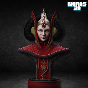 May include: A detailed bust of a woman with a regal appearance, featuring a red and gold headdress and attire. The bust has a red base and is set against a dark background. The text "NORAS 3D" is visible in the upper right corner.