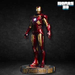 May include: A detailed figurine of Iron Man in a standing pose. The figure is predominantly red and gold, with a glowing blue light in the chest and eyes. The base reads "Iron Man" and "NORAS 3D".