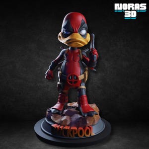 May include: A figurine of a duck-like character in a red and black costume, holding a gun. The figure has a yellow beak and is standing on a base with the word "DUCKPOOL". The figure is a parody of Deadpool.