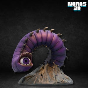 Pode incluir: Uma escultura roxa em forma de verme com um olho grande e dentes afiados. O corpo segmentado tem espinhos escuros e repousa sobre uma base rochosa. O texto "NORAS 3D" está no canto superior direito.