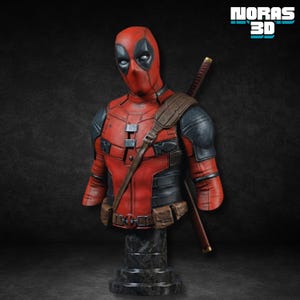 May include: A red and black Deadpool bust with a katana on the back. The bust has a detailed design, including a mask with black eye shapes, a brown strap, and a belt. The base is dark gray with a marble effect. The text "NORAS 3D" is in the upper right corner.