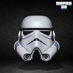 May include: A white Stormtrooper helmet with black and blue detailing. The helmet features a black visor, a detailed mouth area, and blue stripes on the sides. The image includes the text "NORAS 3D".