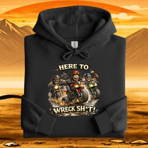May include: Black hooded sweatshirt with a graphic of three cartoon bikers on motorcycles. The text "HERE TO WRECK SH*T!" is printed below the bikers. The background shows a sunset over mountains.