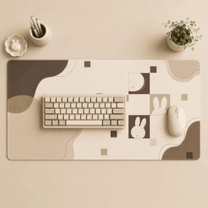 May include: A rectangular desk mat featuring a beige and brown abstract pattern with geometric squares and rabbit silhouettes. A compact mechanical keyboard and a white computer mouse are placed on the mat, accompanied by a small potted plant and a pen holder.
