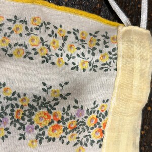 May include: A close-up of a white fabric with a yellow floral pattern. The fabric has a yellow border and is sewn together with a white seam.