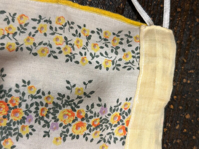 May include: A close-up of a white fabric with a yellow floral pattern. The fabric has a yellow border and is sewn together with a white seam.