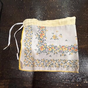 May include: A small white drawstring bag with a yellow trim and a floral pattern. The bag is made of fabric and has a white drawstring.