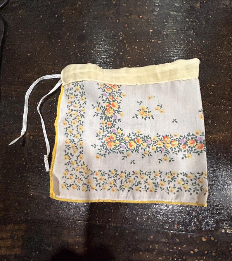 May include: A small white drawstring bag with a yellow trim and a floral pattern. The bag is made of fabric and has a white drawstring.