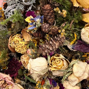 May include: Dried flowers and pine cones in a variety of colors, including yellow, white, pink, purple, and green. The flowers are arranged in a loose, natural style, and the pine cones add a rustic touch.