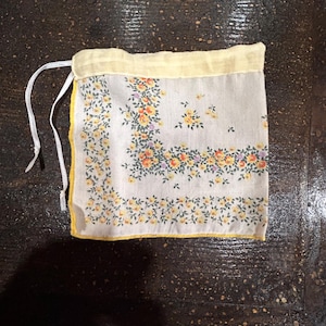 May include: A small white fabric bag with a yellow trim and a floral print. The bag has a drawstring closure.