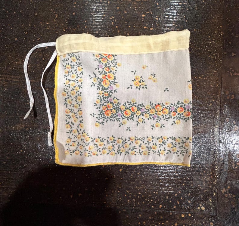 May include: A small white fabric bag with a yellow trim and a floral print. The bag has a drawstring closure.