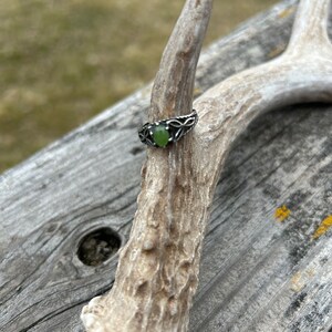 May include: A silver ring with a green gemstone set in a Celtic knot design.