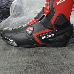May include: Black and red motorcycle boot featuring the "Ducati" logo. The boot has a high-top design with a reinforced heel and toe. The boot is made of leather and has a sleek, modern appearance.