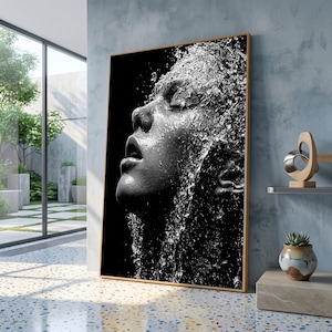 Pode incluir: Uma impressão de arte de parede retangular vertical apresentando um retrato fotográfico em preto e branco de um rosto inclinado para cima com os olhos fechados, coberto por gotas de água em cascata sobre um fundo preto, em uma moldura de madeira clara.