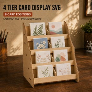 May include: A light-colored wooden 4-tier card display stand with 8 card positions. The display holds various greeting cards featuring botanical and abstract designs, including one with the text 'Happy Birthday' and another with 'thank you'.