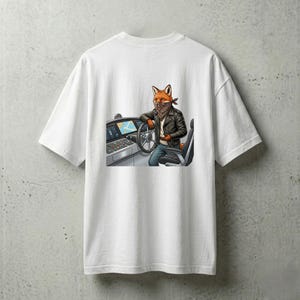 Può includere: T-shirt bianco con un personaggio volpe dei cartoni animati con giacca di pelle e bandana, appoggiato a un volante. La volpe è in un veicolo con cruscotto e sedile. La grafica è dettagliata con colori vivaci.